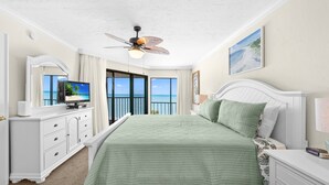 Une chambre avec un grand lit, un ventilateur de plafond, une télévision, une commode et une vue sur l’océan.