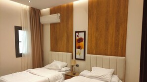 Une chambre d’hôtel avec deux lits, une tête de lit en bois, un appareil de climatisation, une fenêtre avec des rideaux et un tableau au mur.