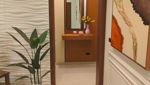 Un couloir avec une porte en bois, un miroir, un lavabo orné d’un vase de fleurs et un grand tableau abstrait accroché au mur.