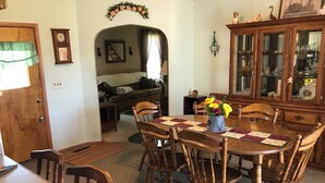 A dining area with a wooden table, chairs, and a floral centerpiece. There is a cabinet with glass doors and a mirror above the table. - Quaint Village home in Allegany.1 mile from St. Bonaventure. (Allegany)