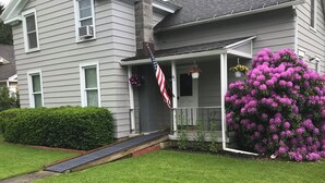 A two-story house with a front porch, a small ramp, and a large bush of purple flowers. - Quaint Village home in Allegany.1 mile from St. Bonaventure. (Allegany)