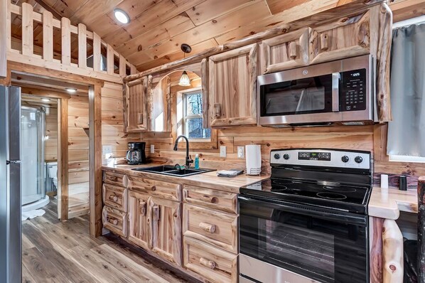 A kitchen with wooden cabinetry, a microwave, a stove, and a sink.