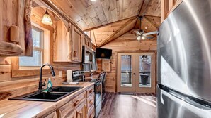 A wooden cabin interior with a kitchen featuring a stainless steel refrigerator, wooden cabinets, and a large window. - New Tiny Home w/Creek Near Gburg (Cosby)