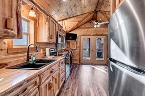 A wooden cabin interior with a kitchen featuring a stainless steel refrigerator, wooden cabinets, and a large window. - New Tiny Home w/Creek Near Gburg (Cosby)