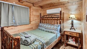 A wooden cabin interior with a bed, a lamp, and a small shelf with decorative items. - New Tiny Home w/Creek Near Gburg (Cosby)