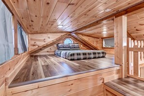 A wooden attic bedroom with a bed, a window, and a sloped ceiling.