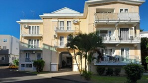 A multi-story residential building with balconies, a central entrance, and a small garden area. - Charming 2-bedroom apartment with AC, WiFi in Flic en Flac, 2 minutes from beach (Flic en Flac)