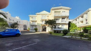 A residential building with a central entrance, multiple balconies, and a parking area with a blue car. - Charming 2-bedroom apartment with AC, WiFi in Flic en Flac, 2 minutes from beach (Flic en Flac)