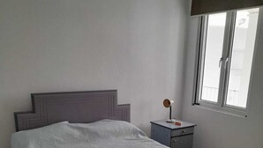 A bedroom with a bed, a nightstand, a window, and a door. - Charming 2-bedroom apartment with AC, WiFi in Flic en Flac, 2 minutes from beach (Flic en Flac)
