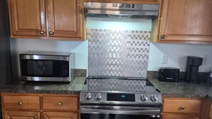 A kitchen with wooden cabinets, a microwave, a stainless steel stove, and a tiled backsplash.