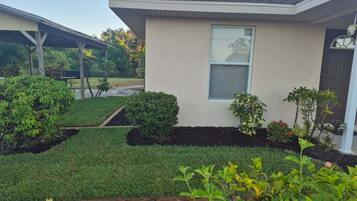A residential house with a well-maintained lawn, a small garden area with various plants, and a clear sky.