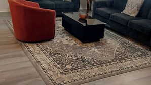 A living room with two sofas, a red chair, a coffee table, a ceiling fan, and a patterned rug.