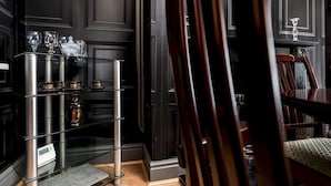 Una habitación con una puerta de madera oscura, un expositor de vidrio con varios objetos, una silla de madera y una pequeña alfombra.