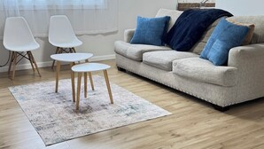 A living room with a beige sofa, two white chairs, a small round table, and a light-colored rug. - 1 Bedroom Urban Loft Suite near EWR, NYC, MetLife! (Newark)