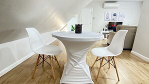 A modern loft apartment with a high ceiling, a dining table with two white chairs, a kitchen area with a TV, and a white door. - 1 Bedroom Urban Loft Suite near EWR, NYC, MetLife! (Newark)