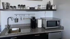 A kitchen with a stainless steel sink, a microwave, and a shelf with kitchen utensils.