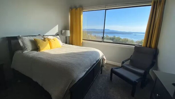 A bedroom with a bed, a chair, a desk, and a large window with curtains.