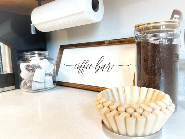 Un comptoir de cuisine aménagé en coin café, comprenant une machine à café, un bocal de grains de café et une pancarte indiquant « coin café ».