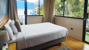 A bedroom with a bed, curtains, a window, and a view of a building.