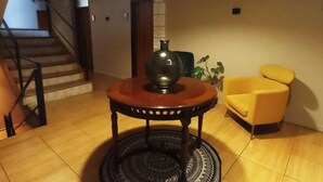 A living room with a staircase, a round table with a vase, a yellow armchair, and a patterned rug.
