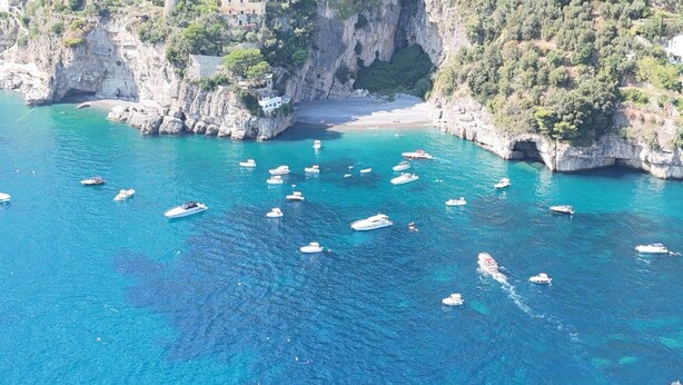 Une zone côtière avec des bateaux sur l’eau et une plage bordée de falaises rocheuses.