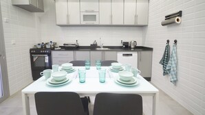 Una cocina compacta con gabinetes blancos, microondas, estufa y lavamanos. Hay una mesa de comedor con platos, tazas y vasos.