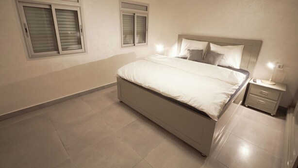 Un dormitorio con cama, mesitas de noche y dos ventanas.