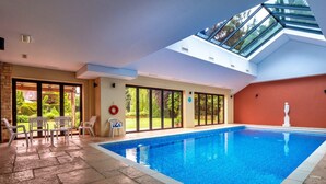 Une piscine intérieure dotée d’une verrière, d’un sol en pierre et offrant une vue sur le jardin extérieur.