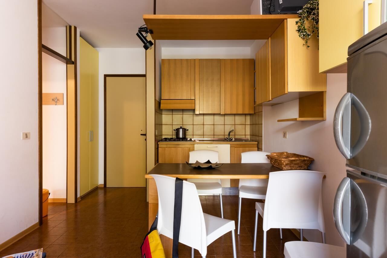 Una cucina compatta con mobili in legno, un frigorifero in acciaio inossidabile e una zona pranzo con sedie bianche.