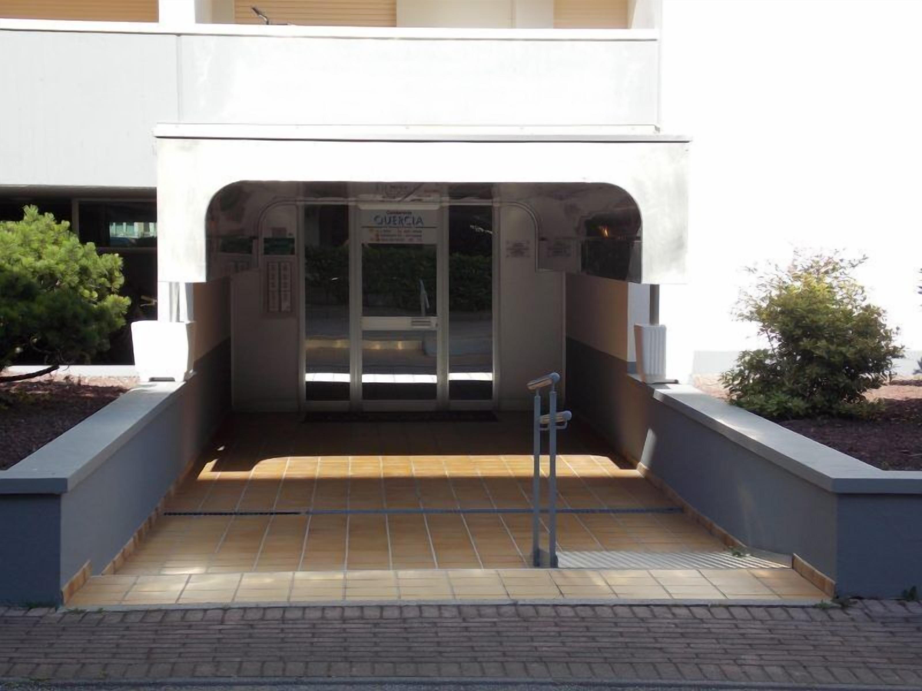Une entrée d’immeuble avec une porte en verre, une enseigne au-dessus de la porte et une rampe menant à l’entrée.