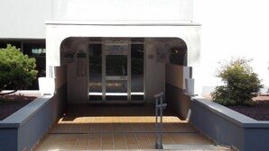 Entrada de un edificio con puerta de cristal, un letrero encima de la puerta y una rampa que conduce a ella.