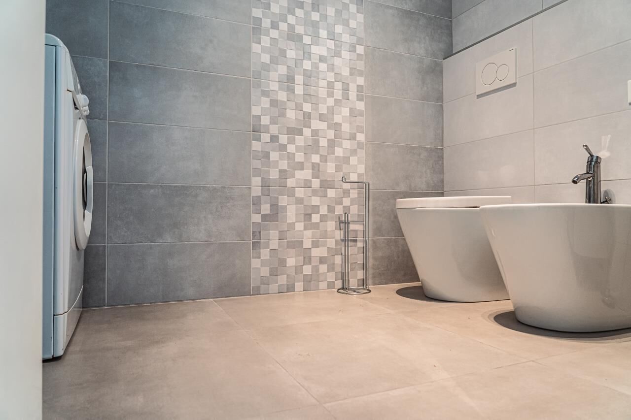 Un baño moderno con baldosas grises, una pared de acento a cuadros, una lavadora y una bañera grande.