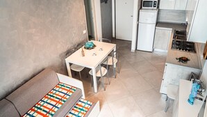A compact kitchen with white appliances, a dining area with a table and chairs, and a sofa with a colorful cushion.