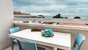 A balcony with a white table and blue chairs, overlooking a coastal view.