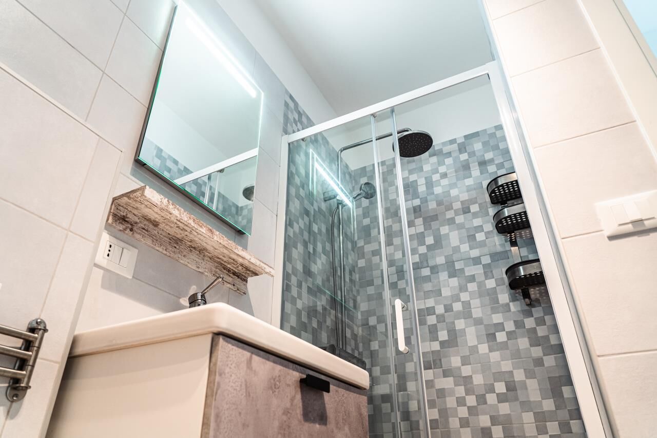 Une salle de bain moderne avec une douche à parois de verre, un miroir au-dessus du lavabo et un sol carrelé.