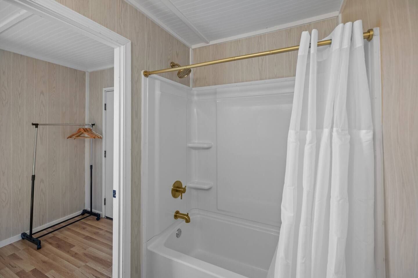 A walk-in shower with a glass door, a gold showerhead, and a white shower curtain.