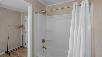 A walk-in shower with a glass door, a gold showerhead, and a white shower curtain.