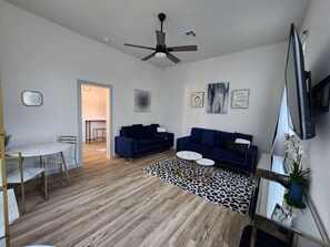 Una sala de estar moderna con ventilador de techo, dos sofás, una mesa de centro y un comedor con mesa y sillas.