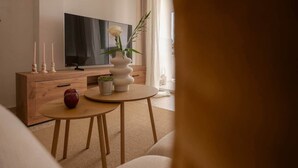 A modern living room with a wooden cabinet, a round table with a vase of flowers, a red apple, and a television on a stand. - Comeback Looking for the Summer (Motril)
