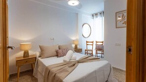 A bedroom with a bed, two bedside tables, a ceiling fan, a mirror, and two chairs. - Comeback Looking for the Summer (Motril)
