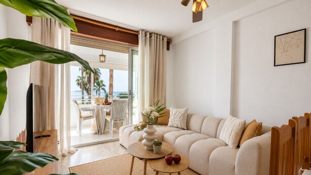 A living room with a sofa, a coffee table, and a TV. There is a view of the outdoors through a glass door. - Comeback Looking for the Summer (Motril)