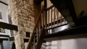 Une chambre avec un mur en pierre, un escalier en bois, un lit et un tapis à motifs.