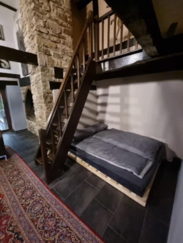 A bedroom with a stone wall, a wooden staircase, a bed, and a patterned rug.