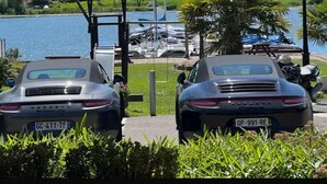 Dos coches aparcados cerca de un muelle con barcos al fondo.