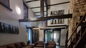 Un área de estar acogedora con un conjunto de sofás, una mesa de centro y una alfombra estampada. Se ven carteles que indican 'LONDON PARIS'.