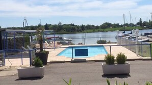 Un espace piscine avec vue sur un lac et des bateaux, entouré d’une clôture et agrémenté de plantes en pot.