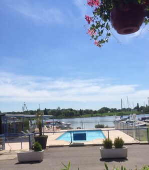 Zona de piscina con vista a un lago y barcos, rodeada por una cerca y plantas en macetas.