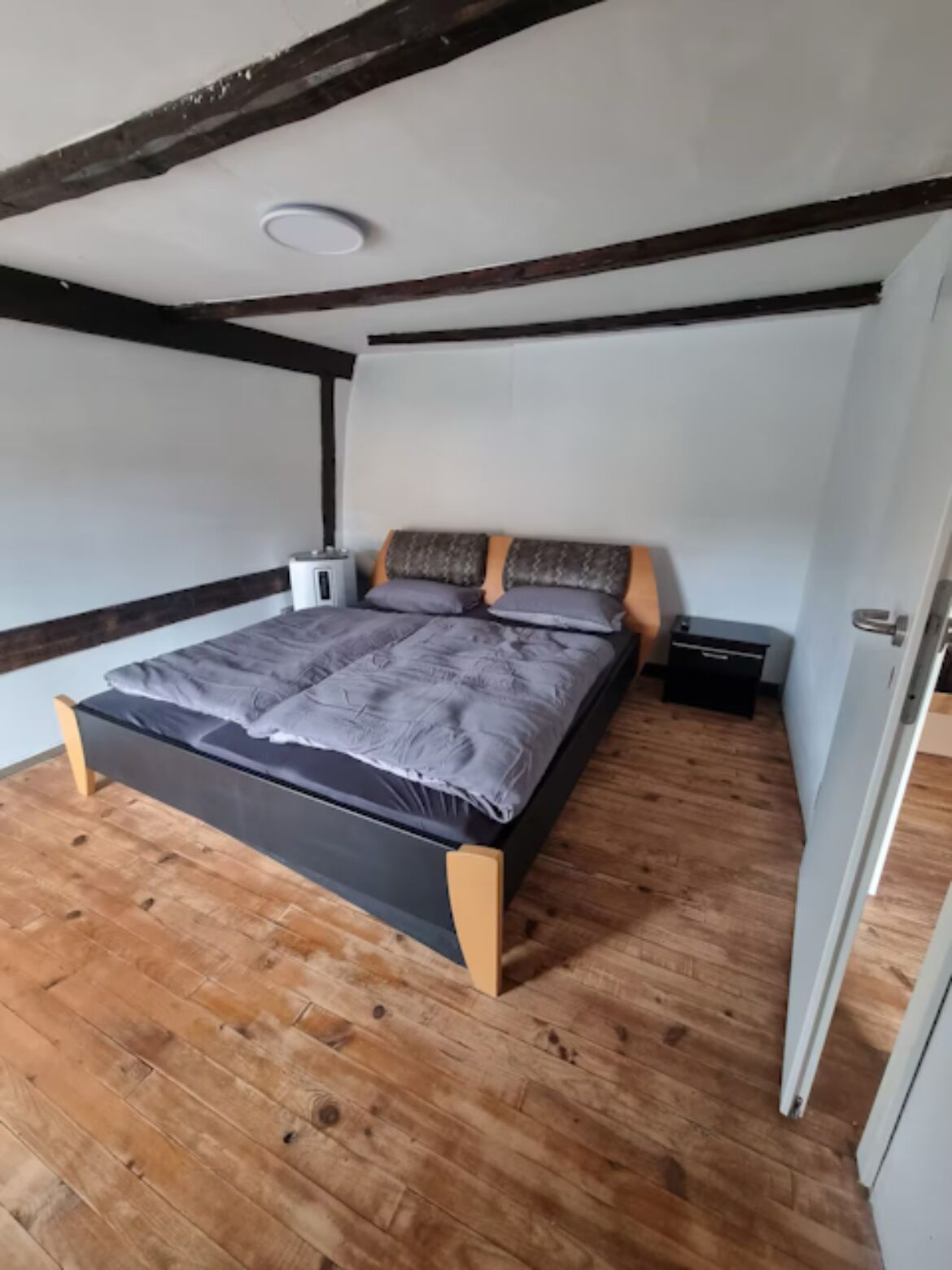 Un dormitorio con piso de madera, una cama con edredón gris y techo blanco.