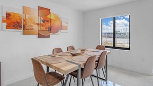 Un comedor con mesa y sillas de madera, un ventanal con vistas, y arte abstracto en la pared.