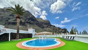 A pool with a stone border, surrounded by artificial grass, with a mountain backdrop. - GOLF SEA&POOL CACTUS VILLA (Buenavista del Norte)